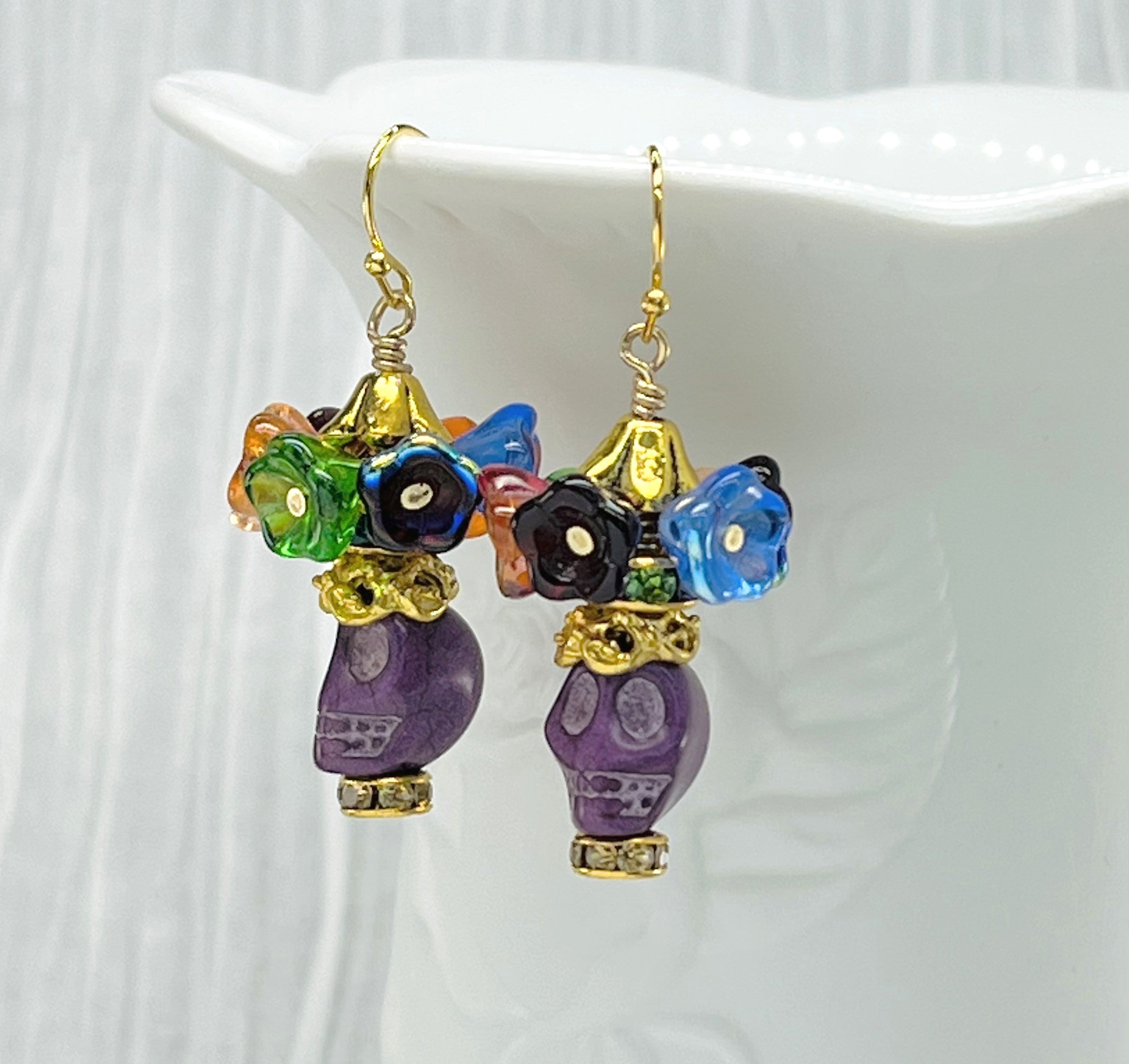 Fun purple Wagnerite skull earrings topped with a row of colorful resin flowers with gold accents