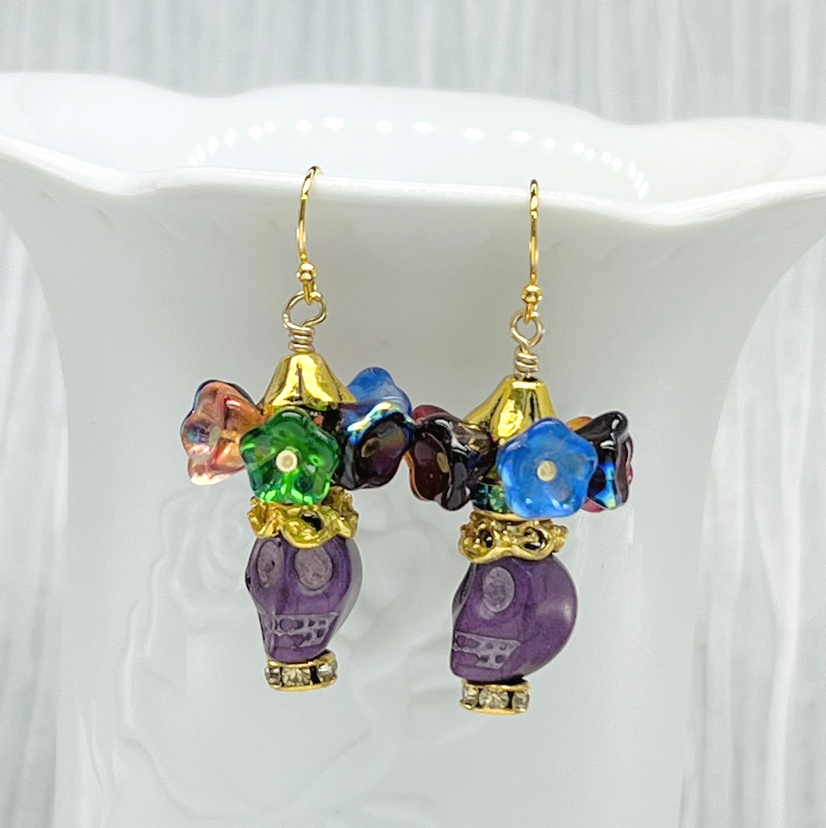 Fun purple Wagnerite skull earrings topped with a row of colorful resin flowers with gold accents