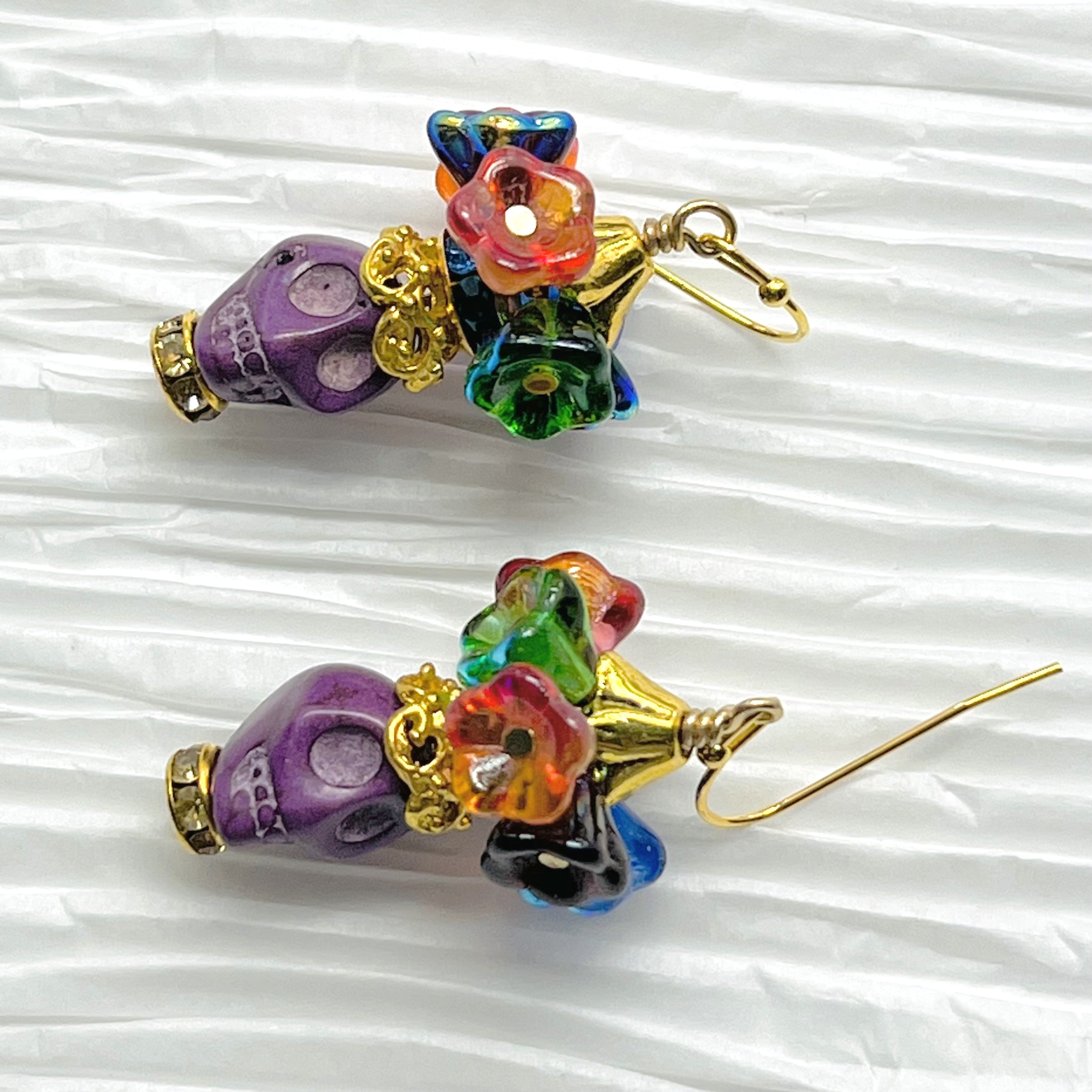 Fun purple Wagnerite skull earrings topped with a row of colorful resin flowers with gold accents