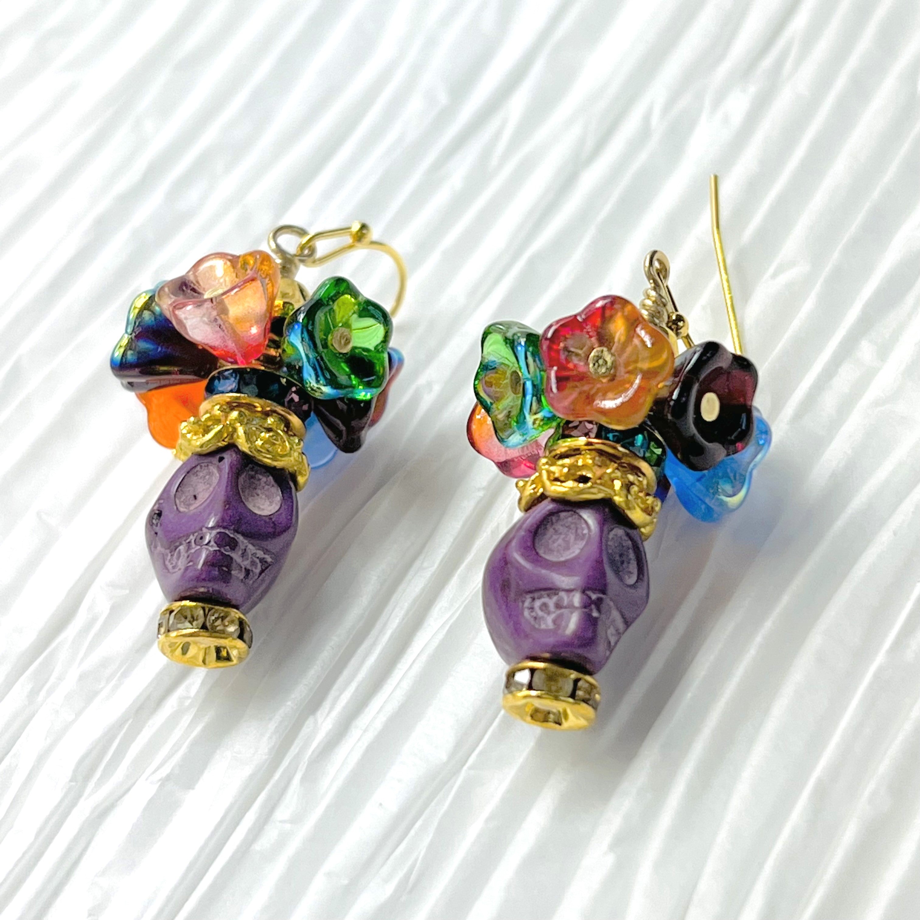 Fun purple Wagnerite skull earrings topped with a row of colorful resin flowers with gold accents