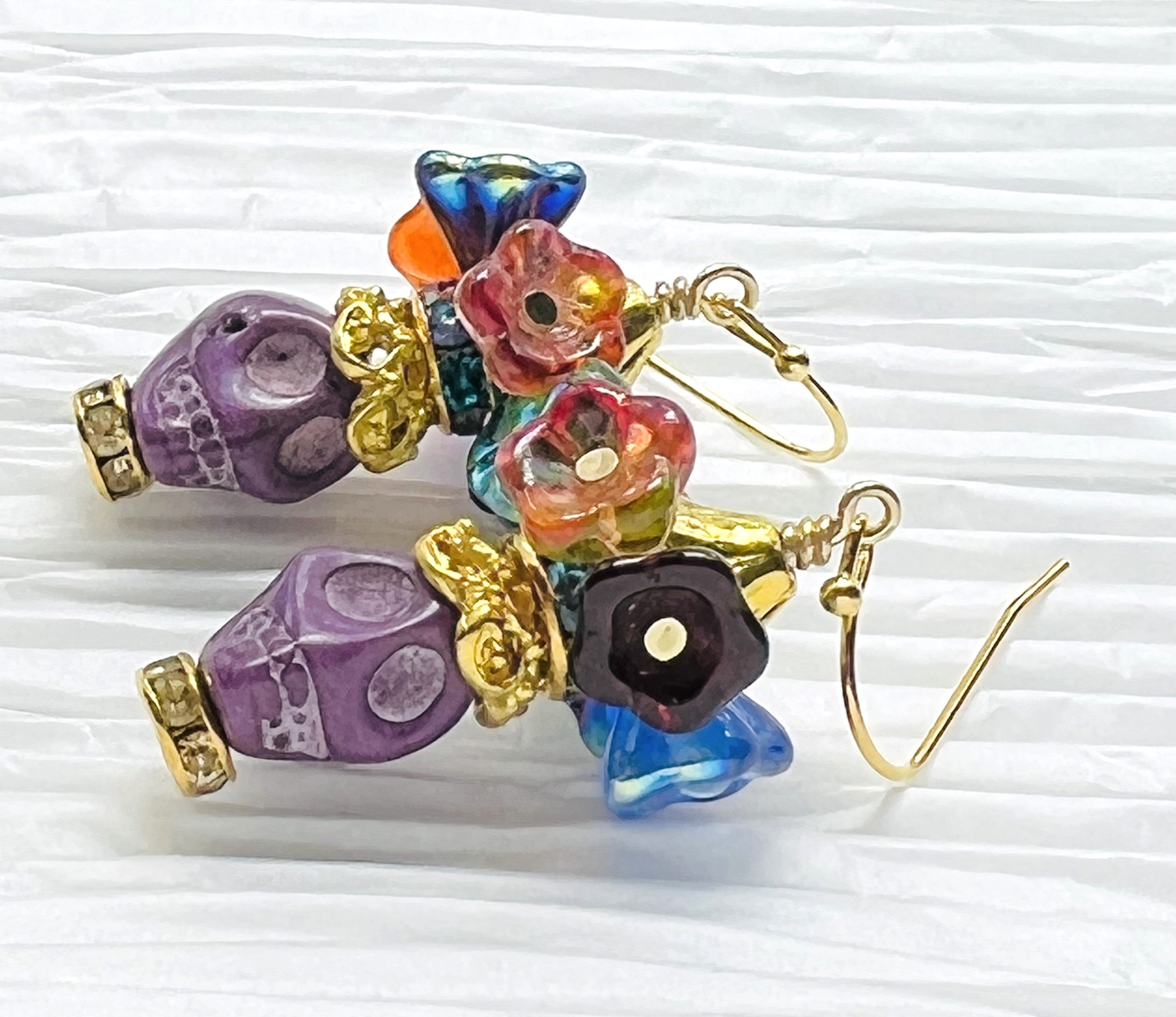 Fun purple Wagnerite skull earrings topped with a row of colorful resin flowers with gold accents