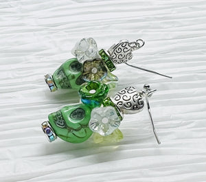 Pretty green Wagnerite skull earrings topped with a row of resin flowers in white, green and silver