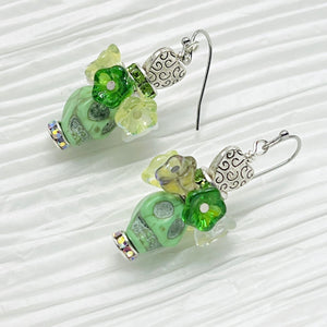 Pretty green Wagnerite skull earrings topped with a row of resin flowers in white, green and silver