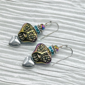 Colorful iridescent glass skulls top a silver heart and are crowned by a sparkling turquoise rhinestone rondel