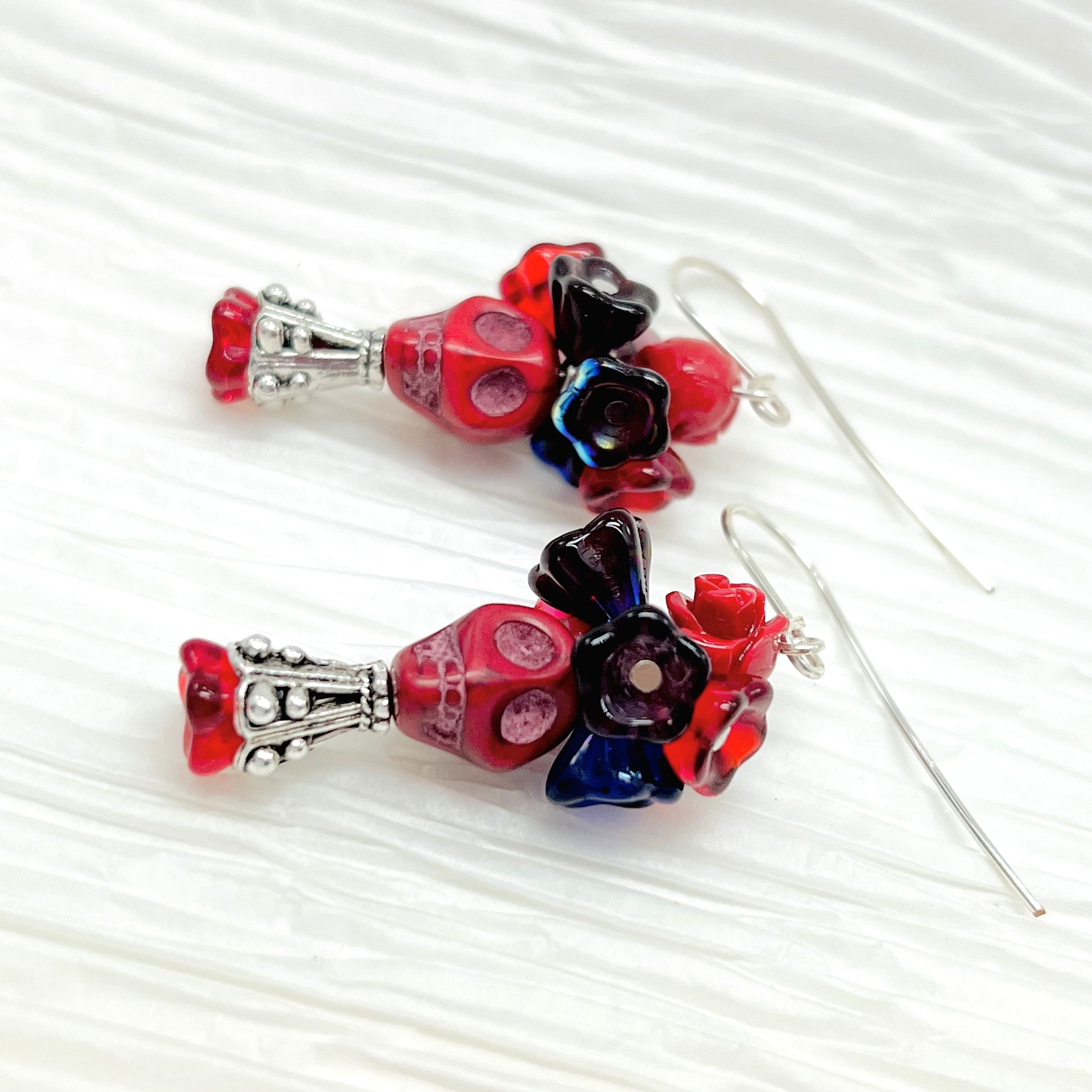 Passionate red Wagnerite skull earrings topped with a row of colorful resin flowers in red, blue and purple