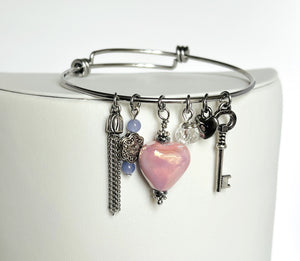 Silver bangle bracelet with pink ceramic heart, key, and chain tassel charms