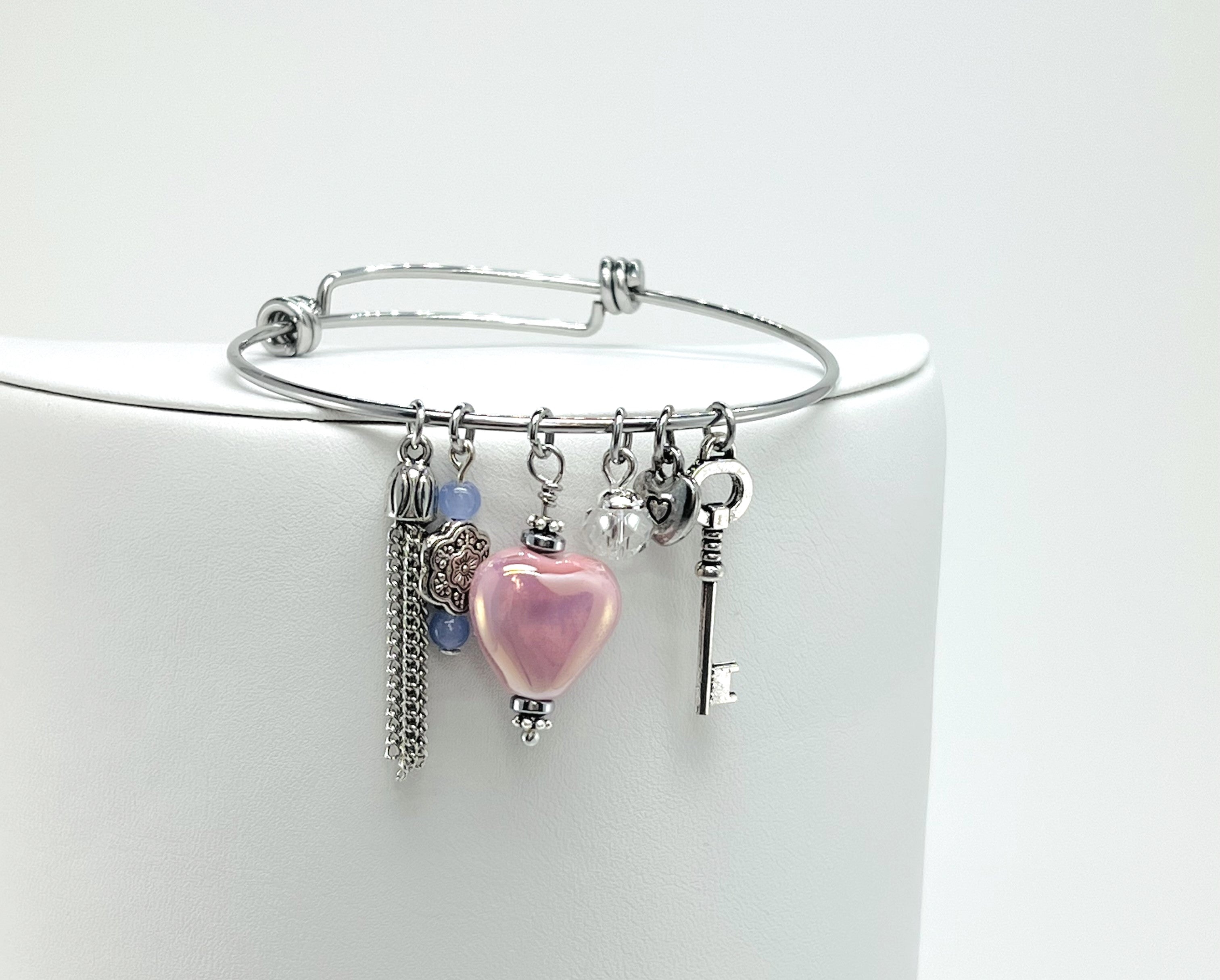 Silver bangle bracelet with pink ceramic heart, key, and chain tassel charms