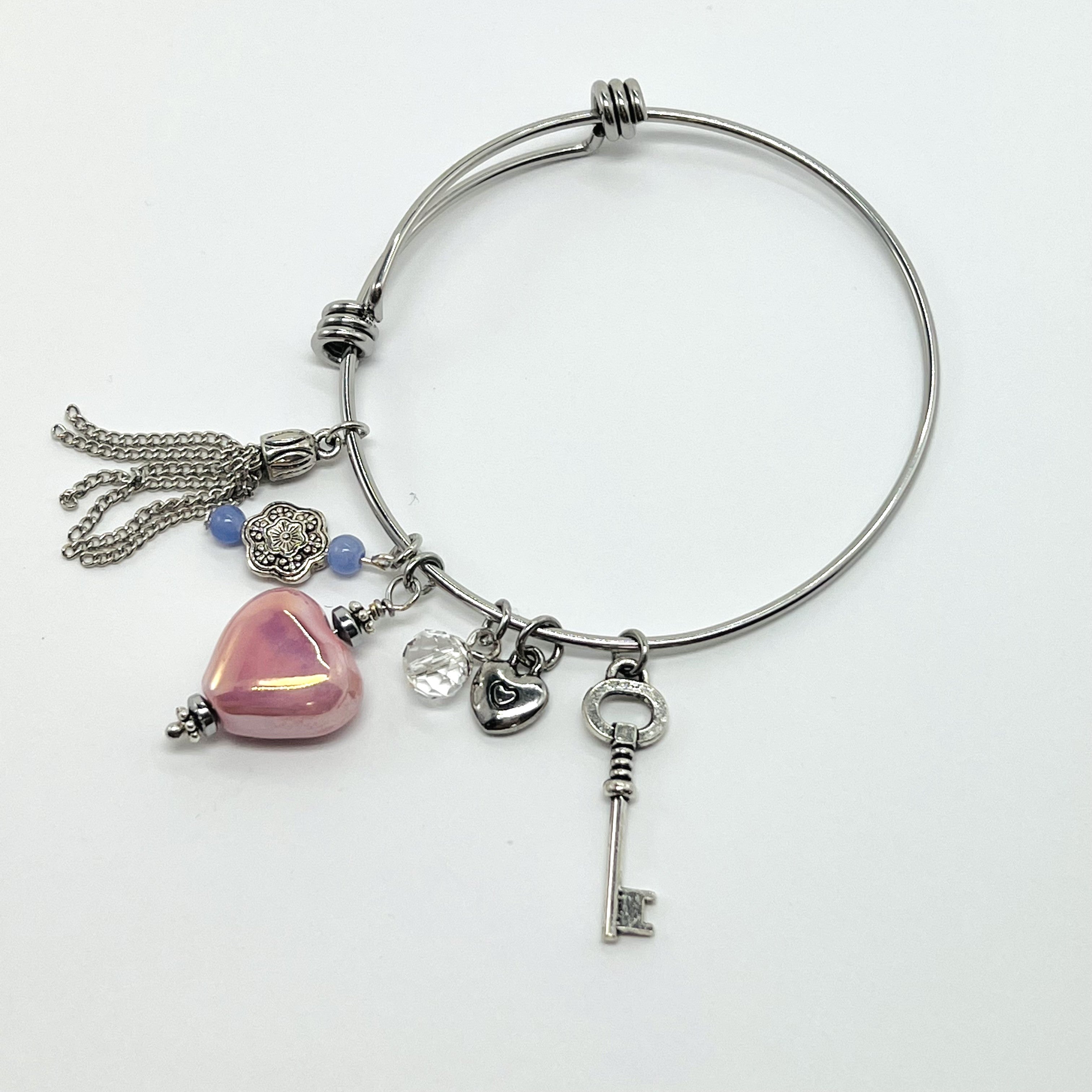 Silver bangle bracelet with pink ceramic heart, key, and chain tassel charms