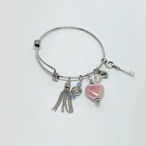 Silver bangle bracelet with pink ceramic heart, key, and chain tassel charms