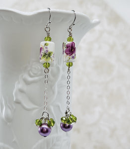 Earrings with a pink and purple ceramic floral bead and green cut glass and lavender glass beads with silver metal elements