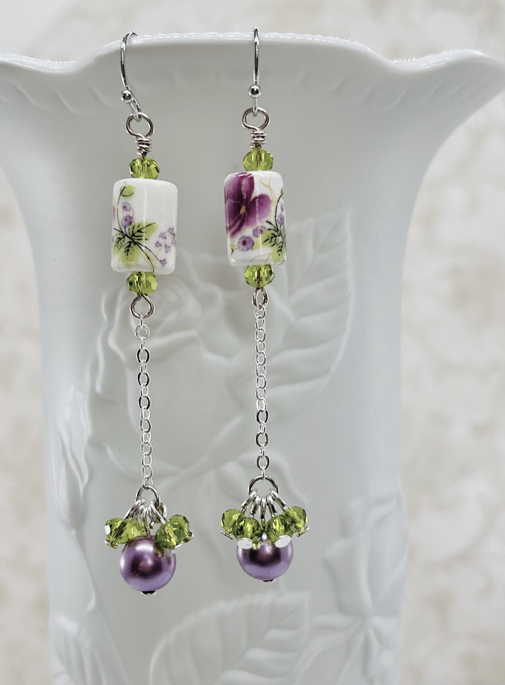 Earrings with a pink and purple ceramic floral bead and green cut glass and lavender glass beads with silver metal elements