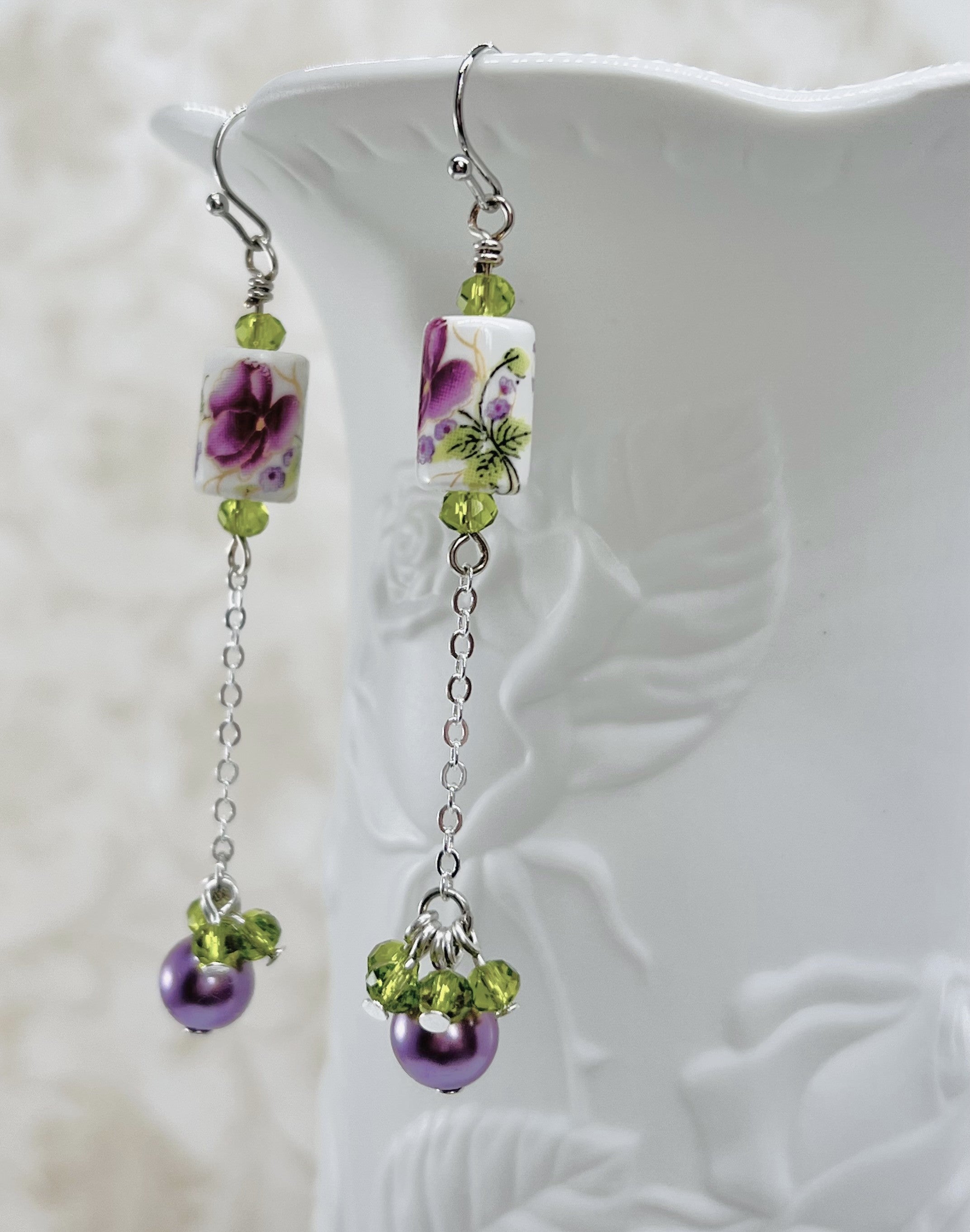 Earrings with a pink and purple ceramic floral bead and green cut glass and lavender glass beads with silver metal elements