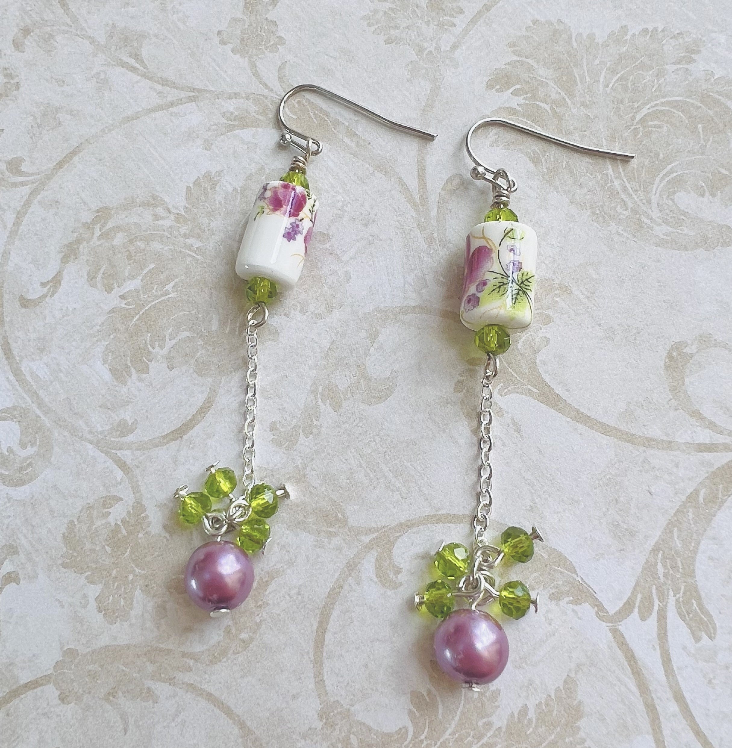 Earrings with a pink and purple ceramic floral bead and green cut glass and lavender glass beads with silver metal elements