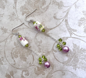 Earrings with a pink and purple ceramic floral bead and green cut glass and lavender glass beads with silver metal elements