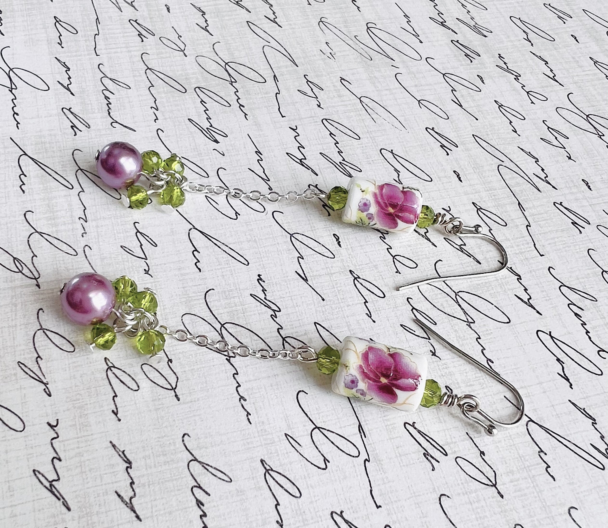 Earrings with a pink and purple ceramic floral bead and green cut glass and lavender glass beads with silver metal elements