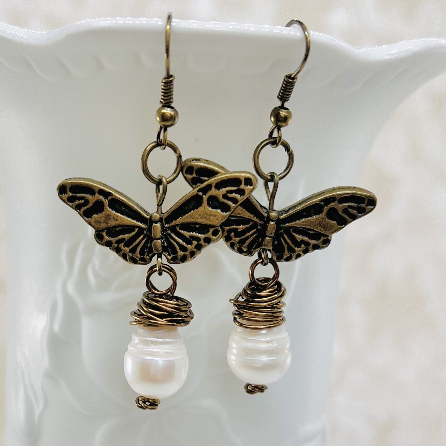 Earrings with a large fresh water pearl and a butterfly that dangle from an antique brass ear wire.