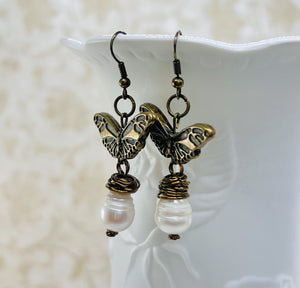 Earrings with a large fresh water pearl and a butterfly that dangle from an antique brass ear wire.