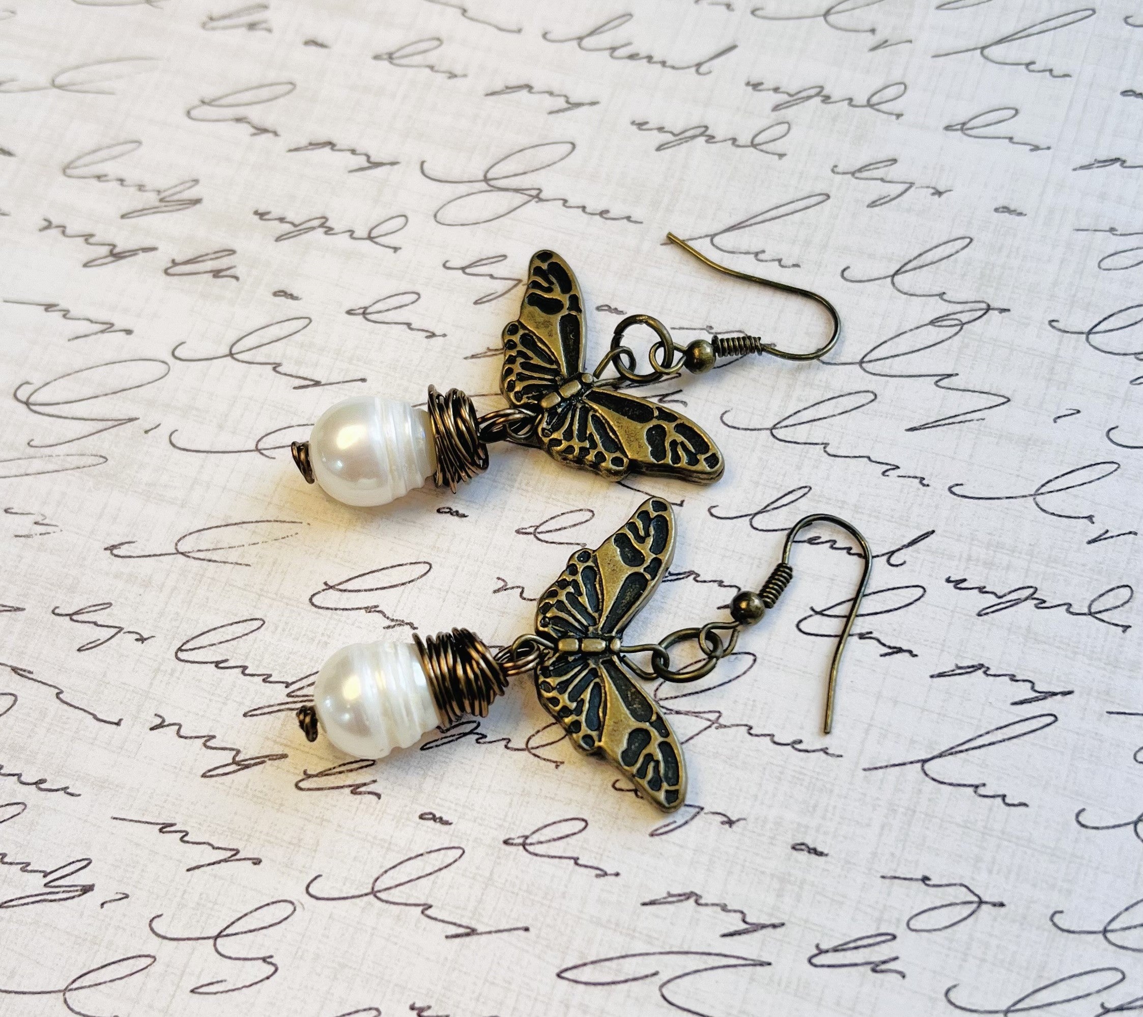 Earrings with a large fresh water pearl and a butterfly that dangle from an antique brass ear wire.