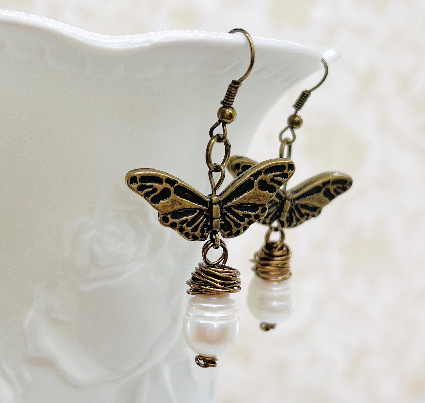 Earrings with a large fresh water pearl and a butterfly that dangle from an antique brass ear wire.